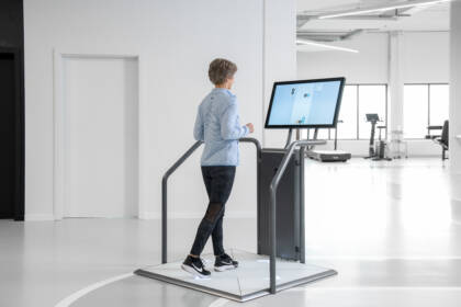 Ältere Frau trainiert an einem interaktiven Bildschirm-Trainingsgerät für Gleichgewicht und Kognition im hellen Trainingsraum des Gesundheitszentrums GUT